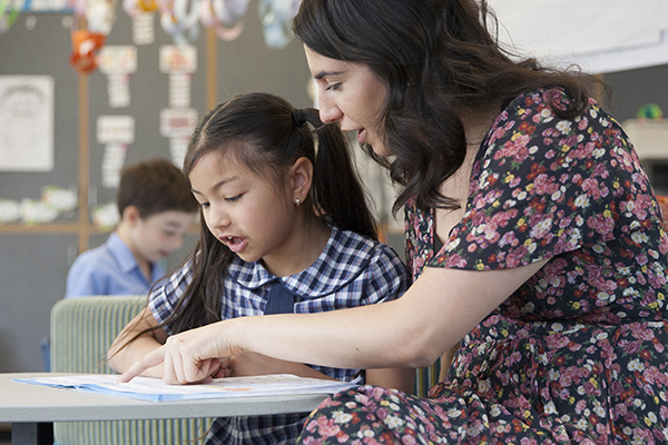 A teacher helps a primary school student with her school work