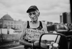 Homeless man holds sign that reads 'Struggling Can you Help' - Photo by Zoe Vandewater by Unsplash