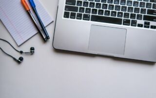 Laptop, pens, notepad and ear buds on a desk - Photo by Maya Maceka on Unsplash